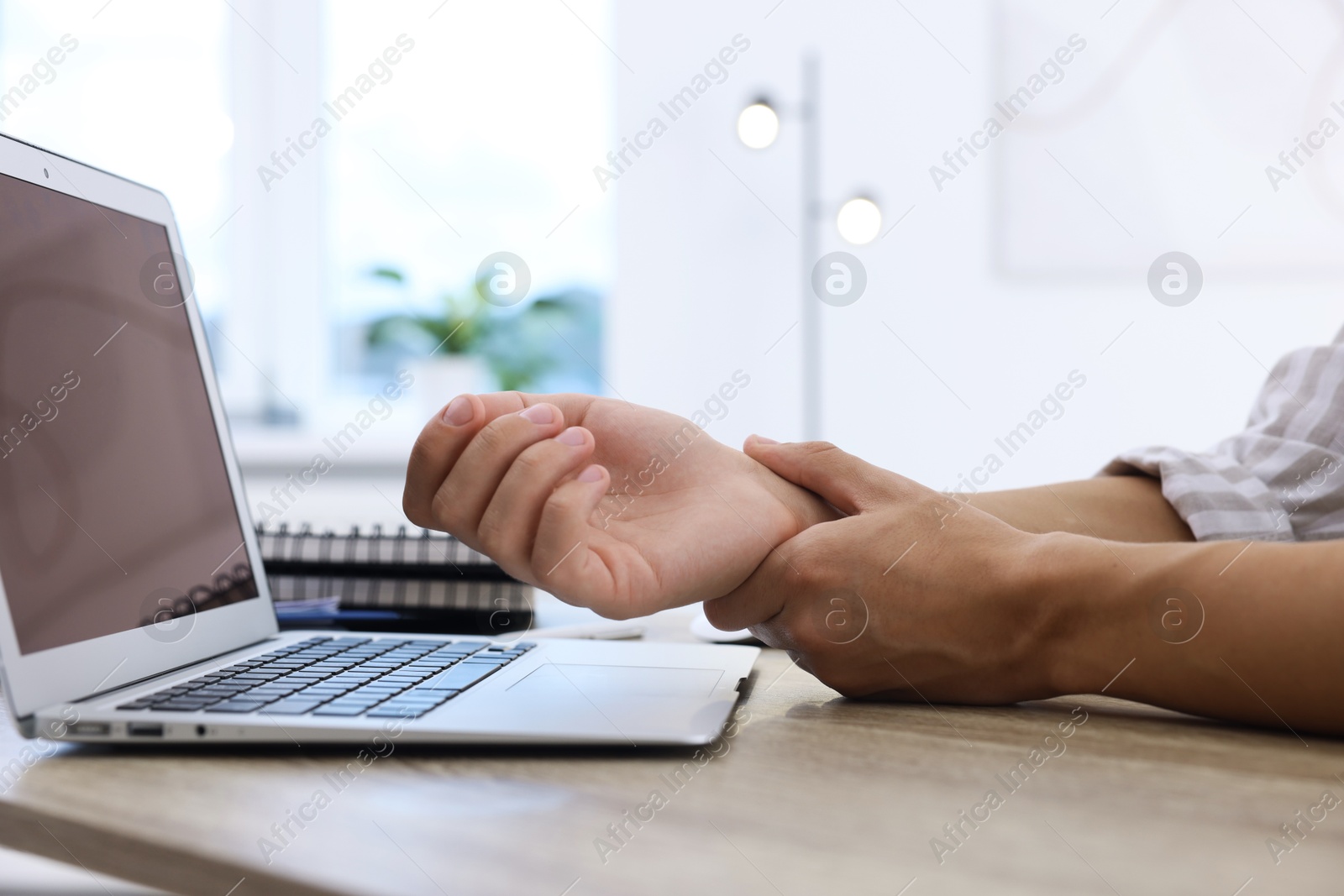 Photo of Man suffering from pain in wrist while working on laptop at table indoors, closeup. Carpal tunnel syndrome