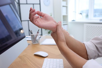 Photo of Man suffering from pain in wrist while working on computer at table indoors, closeup. Carpal tunnel syndrome