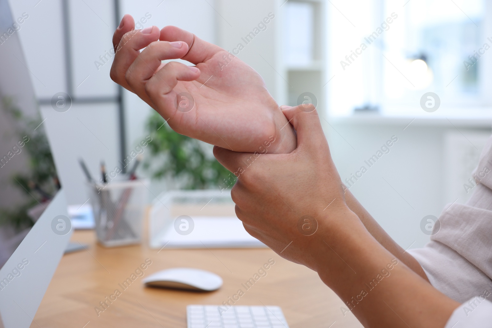 Photo of Man suffering from pain in wrist while working on computer at table indoors, closeup. Carpal tunnel syndrome