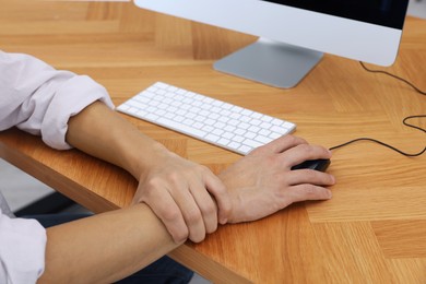 Photo of Man suffering from pain in wrist while using computer mouse at table indoors, closeup. Carpal tunnel syndrome