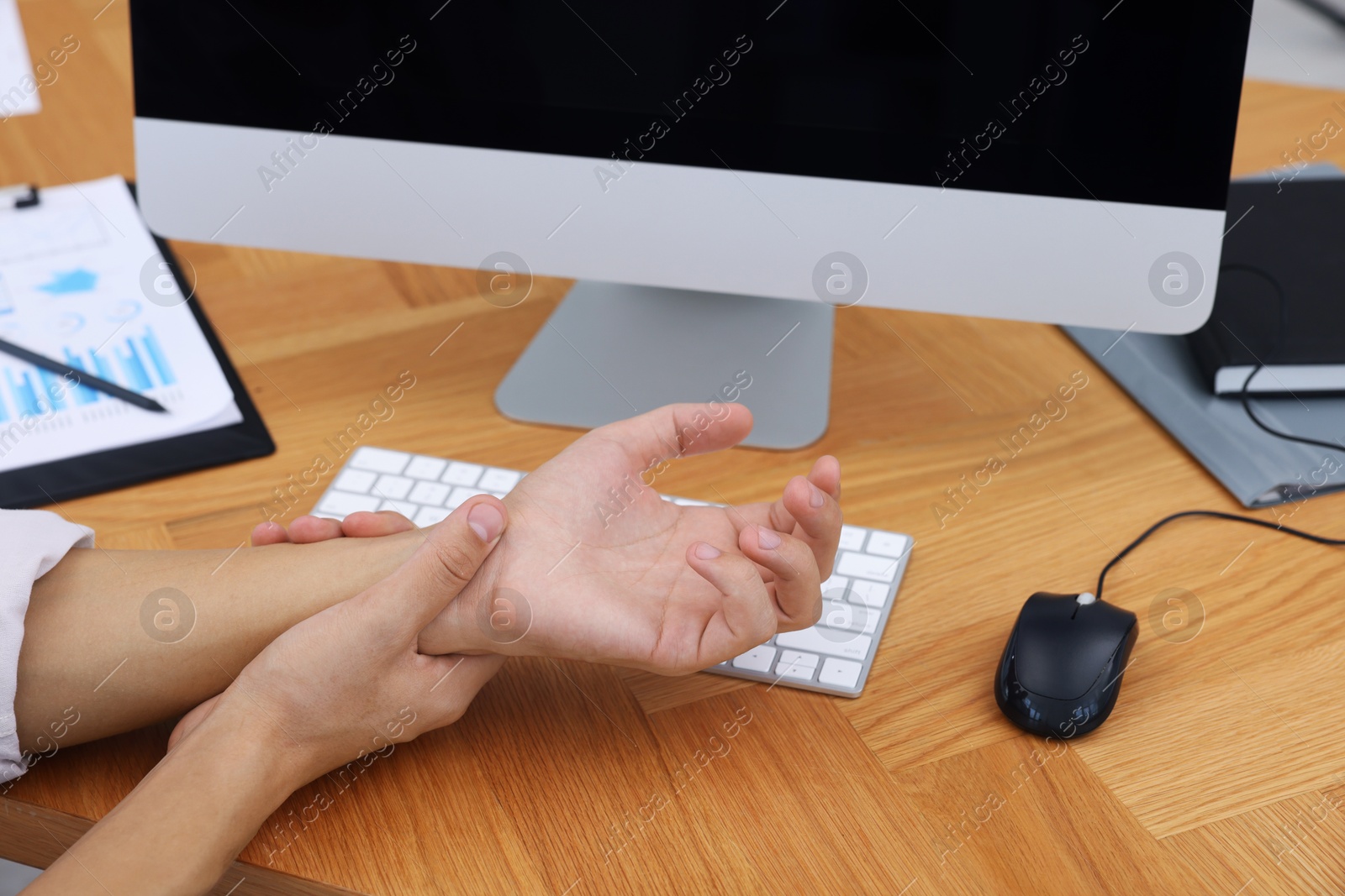 Photo of Man suffering from pain in wrist while working on computer at wooden table, closeup. Carpal tunnel syndrome