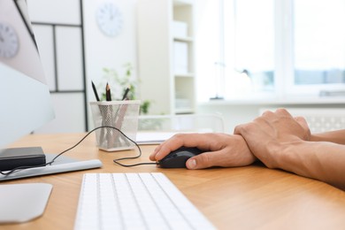 Photo of Man suffering from pain in wrist while using computer mouse at table indoors, closeup. Carpal tunnel syndrome