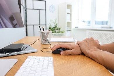 Photo of Man suffering from pain in wrist while using computer mouse at table indoors, closeup. Carpal tunnel syndrome