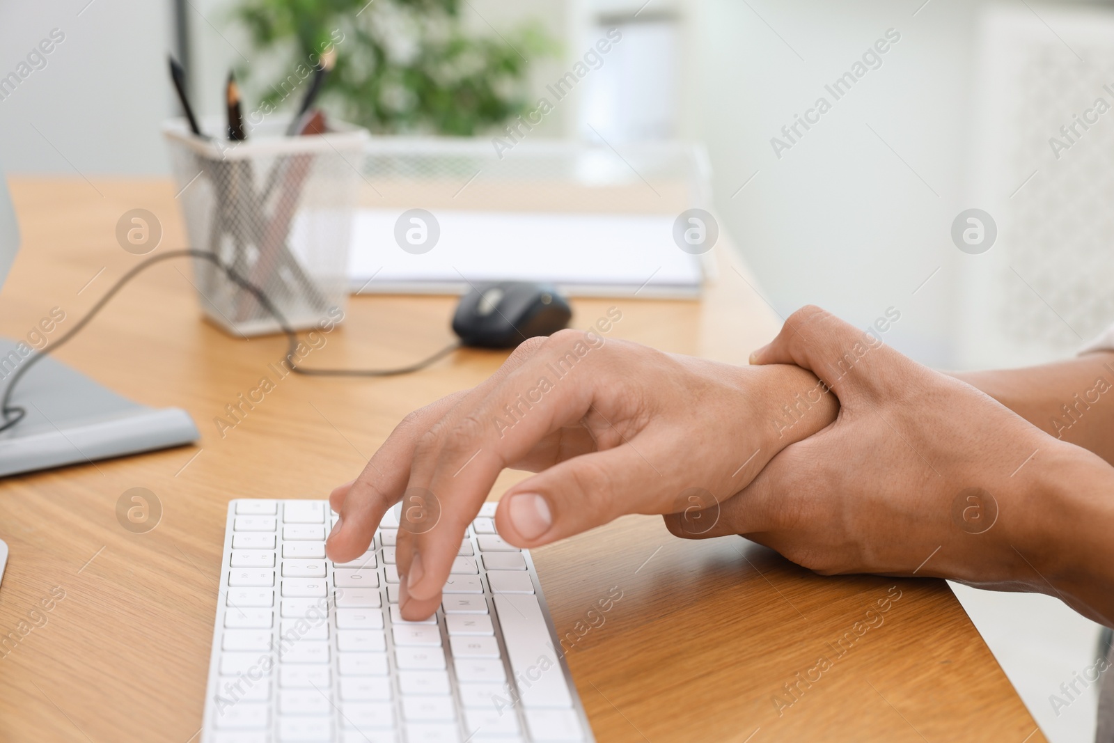 Photo of Man suffering from pain in wrist while working on computer at table indoors, closeup. Carpal tunnel syndrome