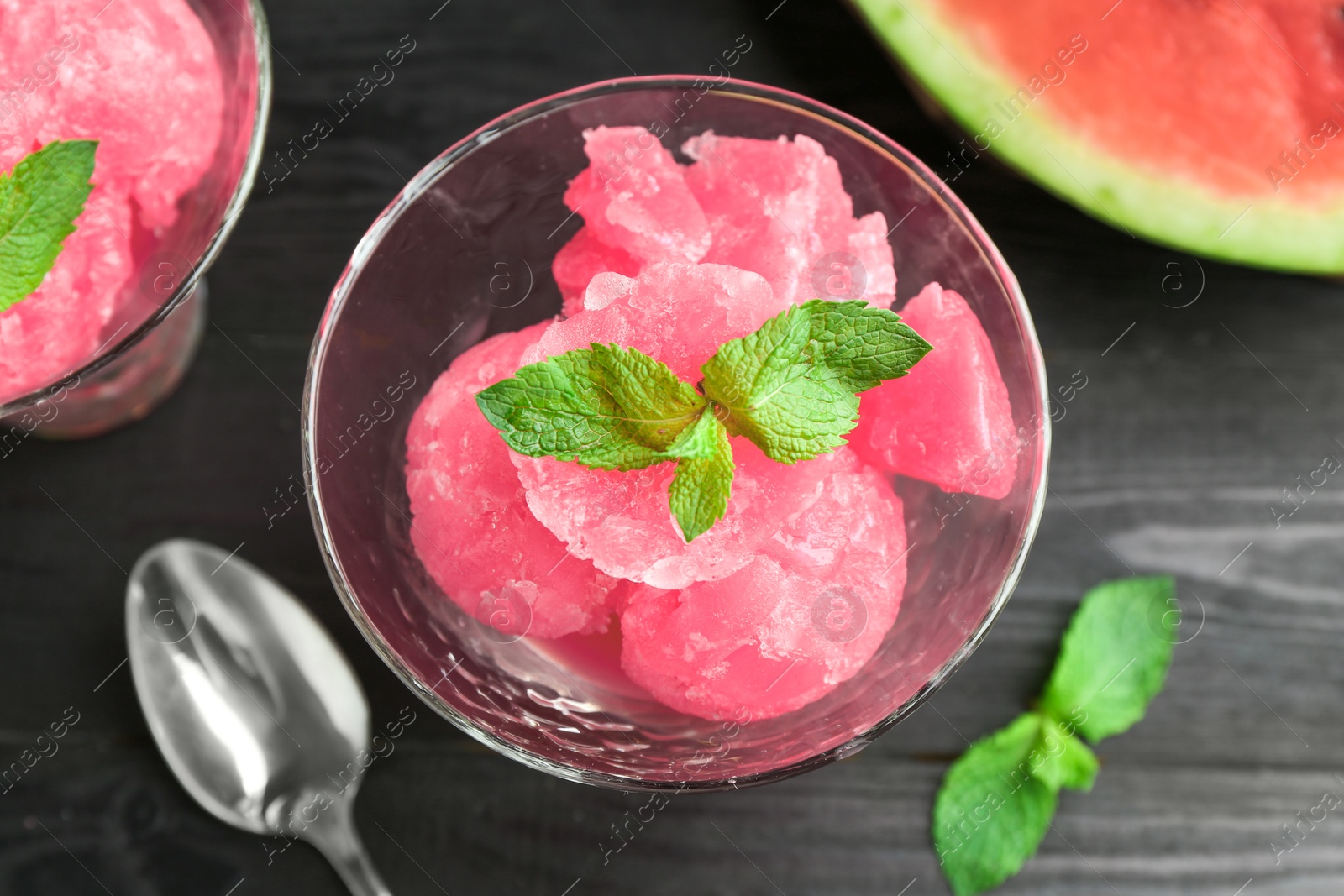 Photo of Tasty watermelon sorbet with mint in glass dessert bowl and spoon on black table, flat lay