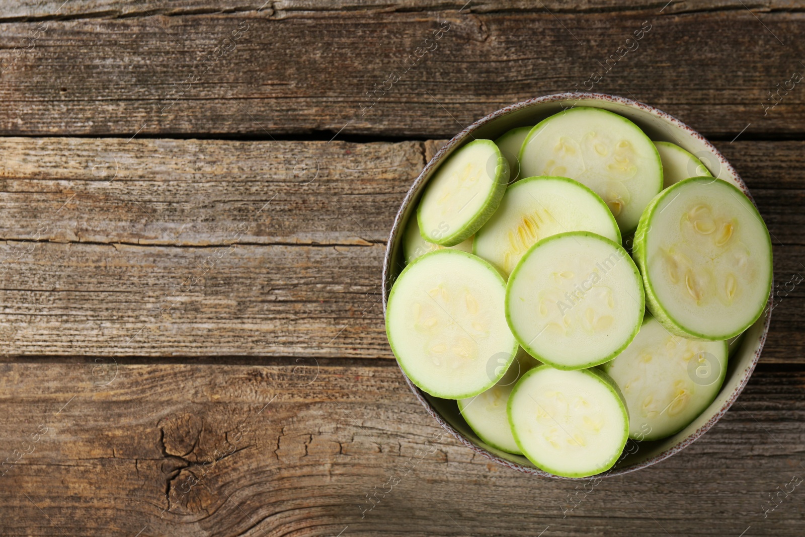 Photo of Fresh cut zucchinis in bowl on wooden table, top view. Space for text