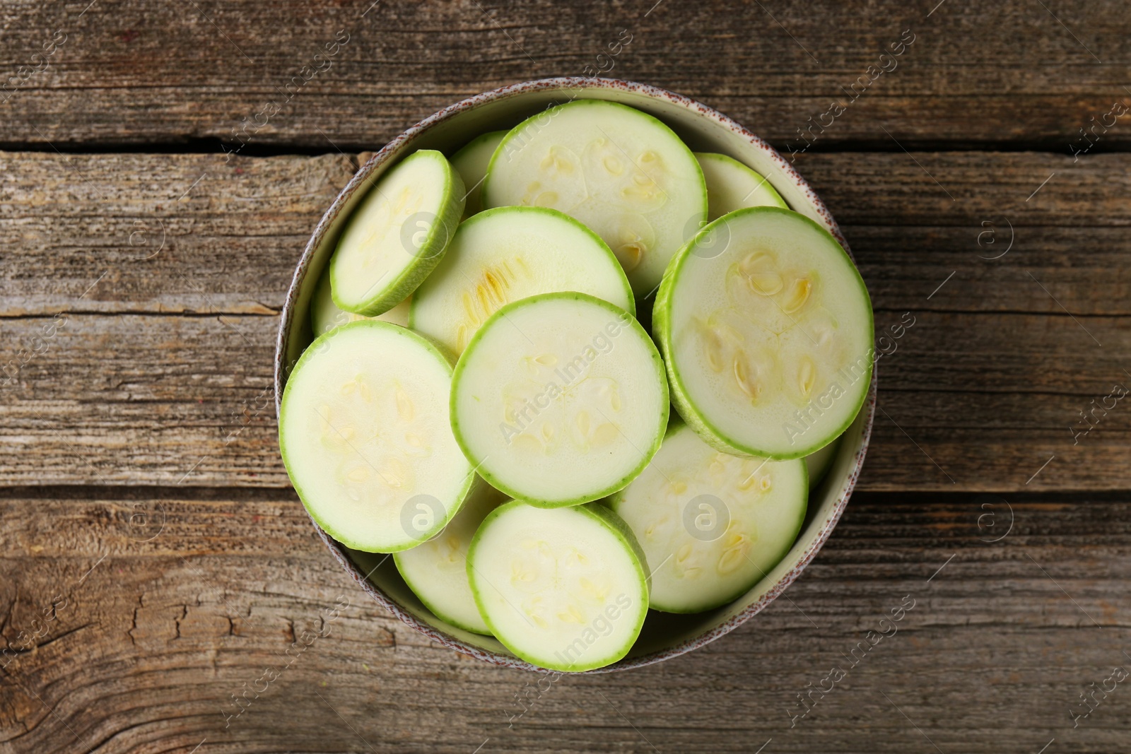 Photo of Fresh cut zucchinis in bowl on wooden table, top view