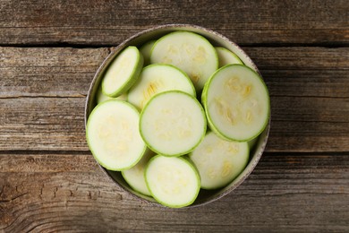 Photo of Fresh cut zucchinis in bowl on wooden table, top view