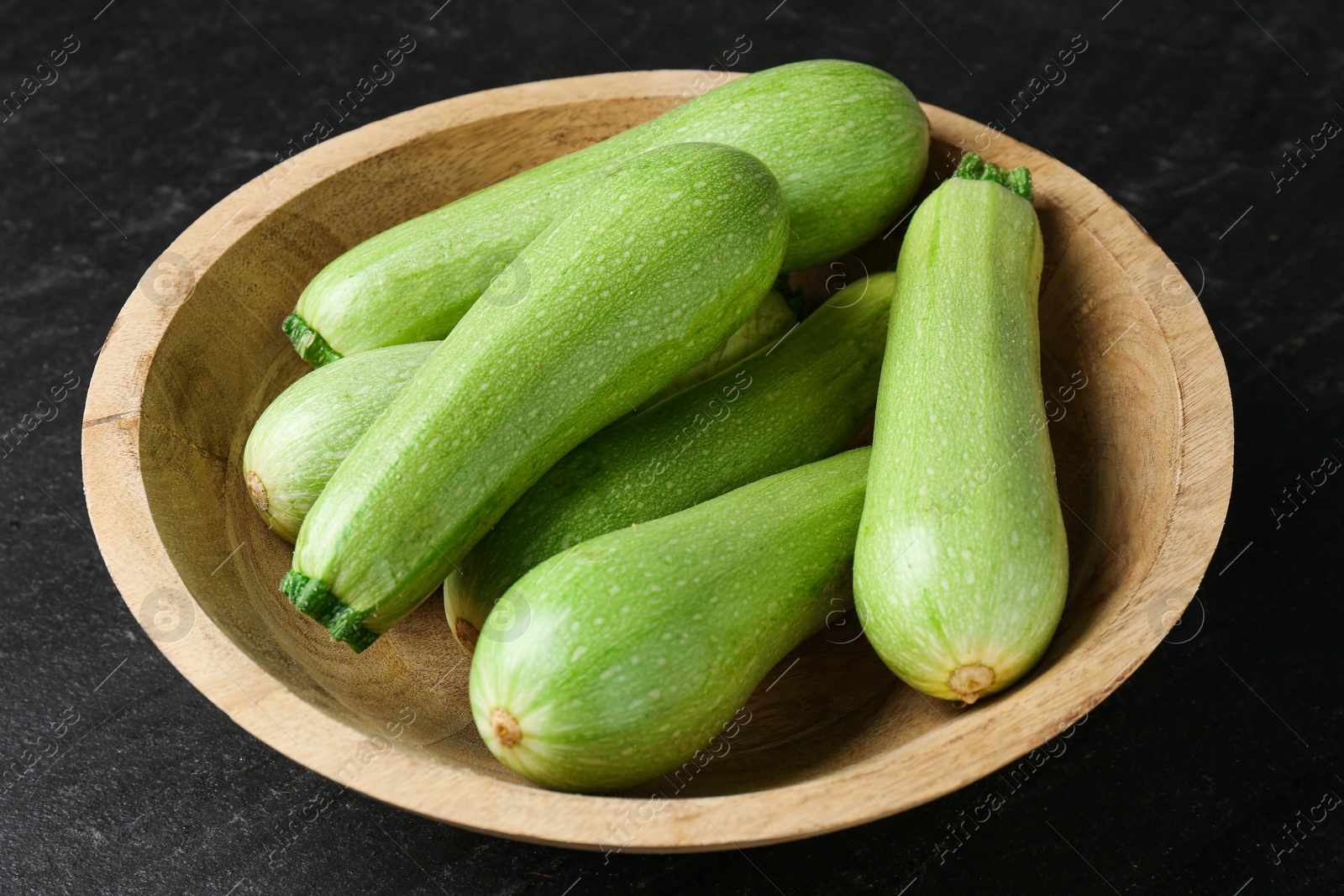 Photo of Fresh zucchinis in bowl on dark table, closeup