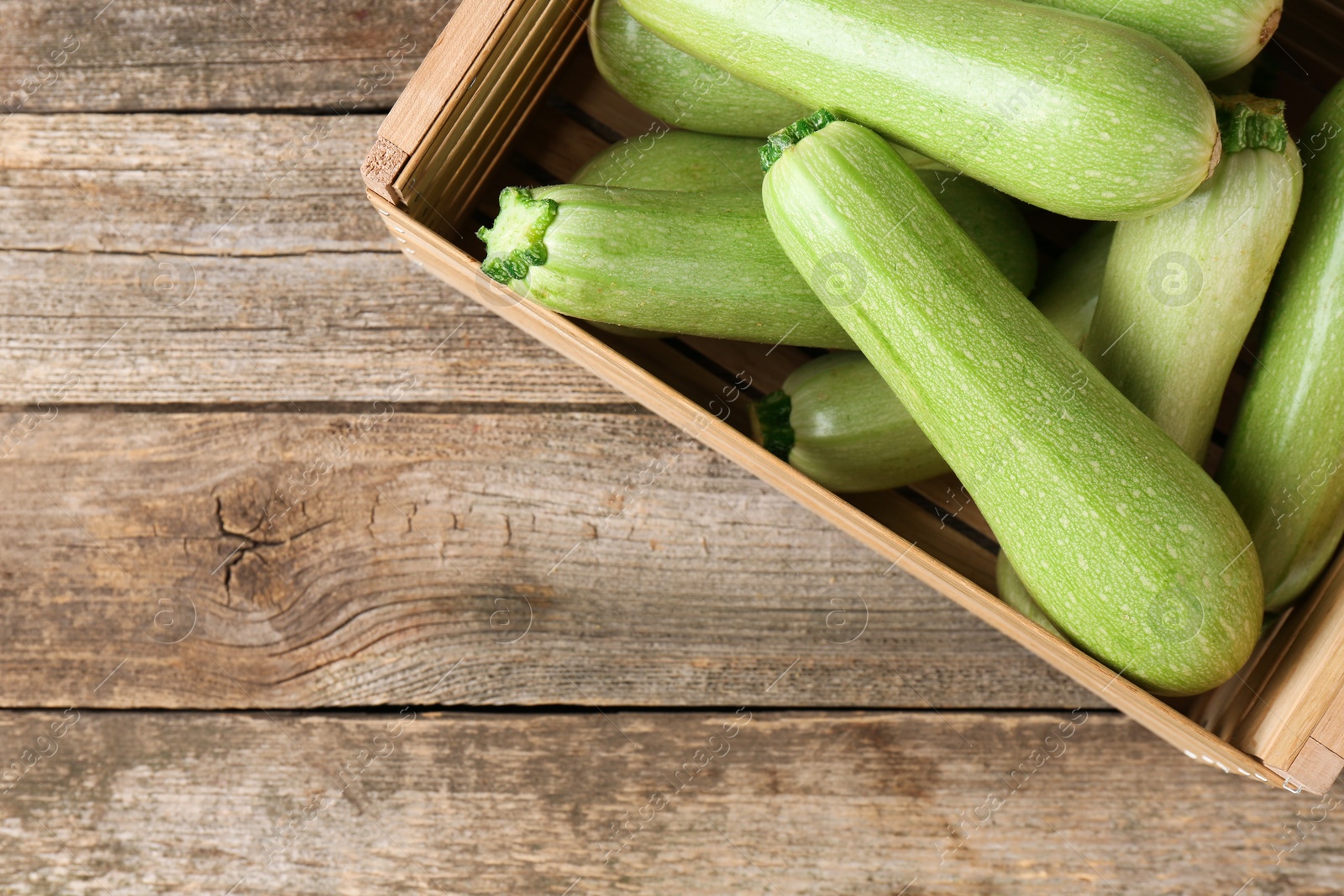 Photo of Crate with fresh zucchinis on wooden table, top view. Space for text