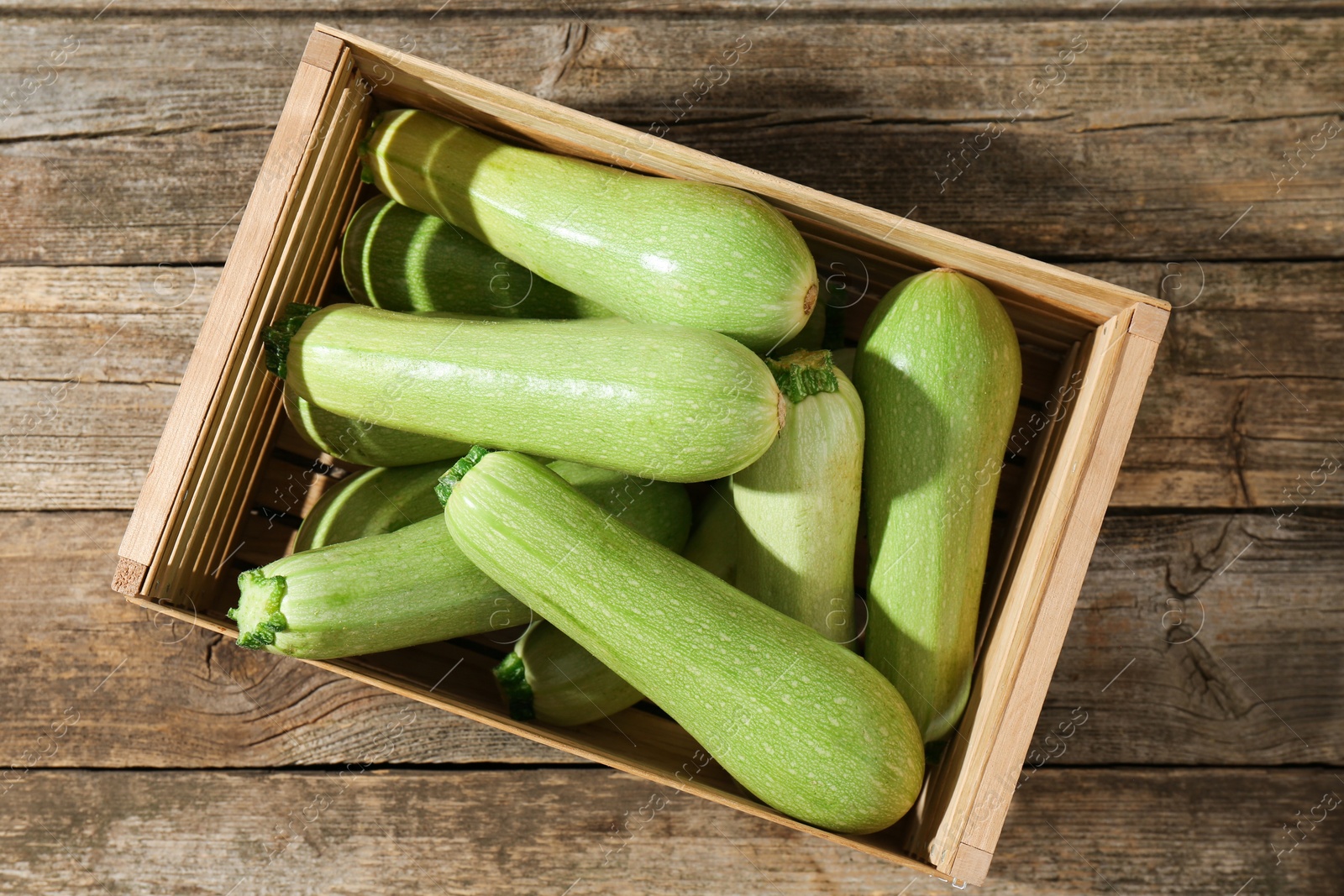 Photo of Crate with fresh zucchinis on wooden table, top view