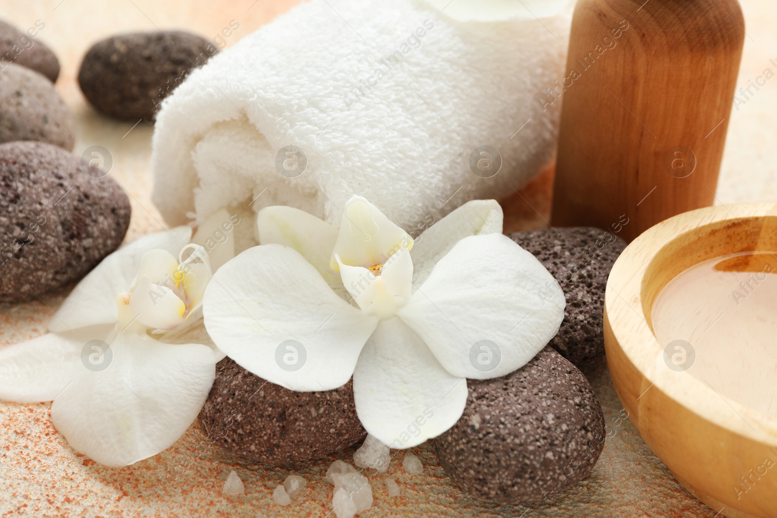 Photo of Spa stones, beautiful orchid flowers, sea salt and cosmetic products on beige textured surface, closeup