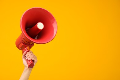 Photo of Woman holding megaphone speaker on orange background, closeup. Space for text