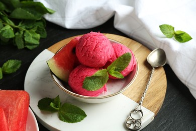 Photo of Scoops of tasty watermelon sorbet with mint, fresh fruit in bowl and spoon on grey textured table