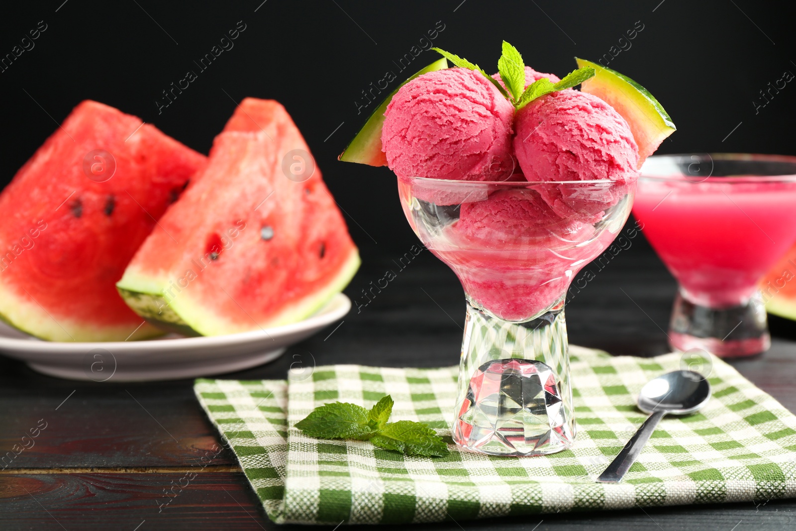 Photo of Scoops of tasty watermelon sorbet with mint, fresh fruit in glass dessert bowl and spoon on wooden table