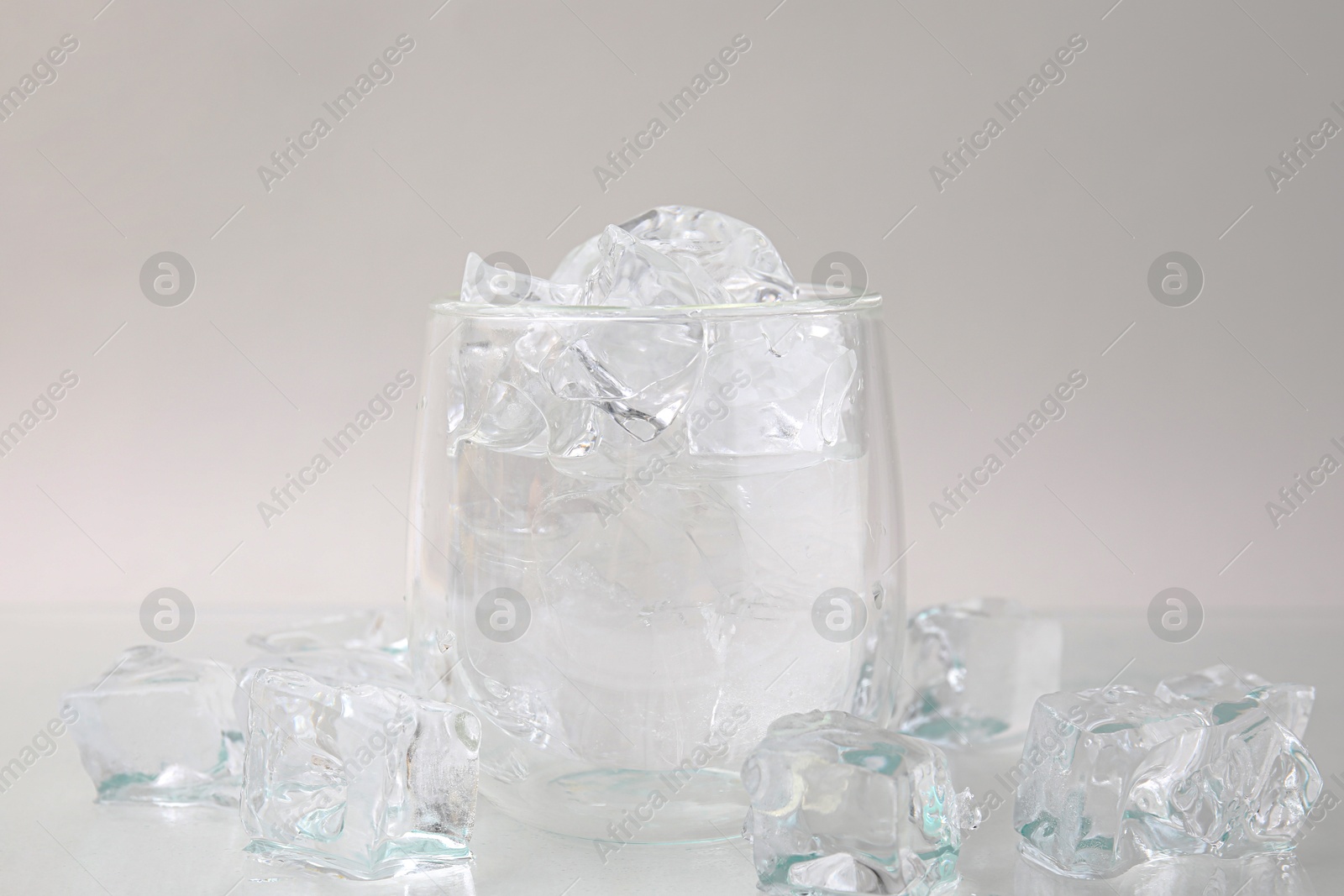 Photo of Refreshing water in glass with ice cubes on light background