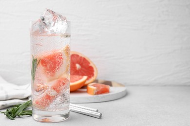 Photo of Refreshing water with grapefruit and rosemary in glass on light table, space for text