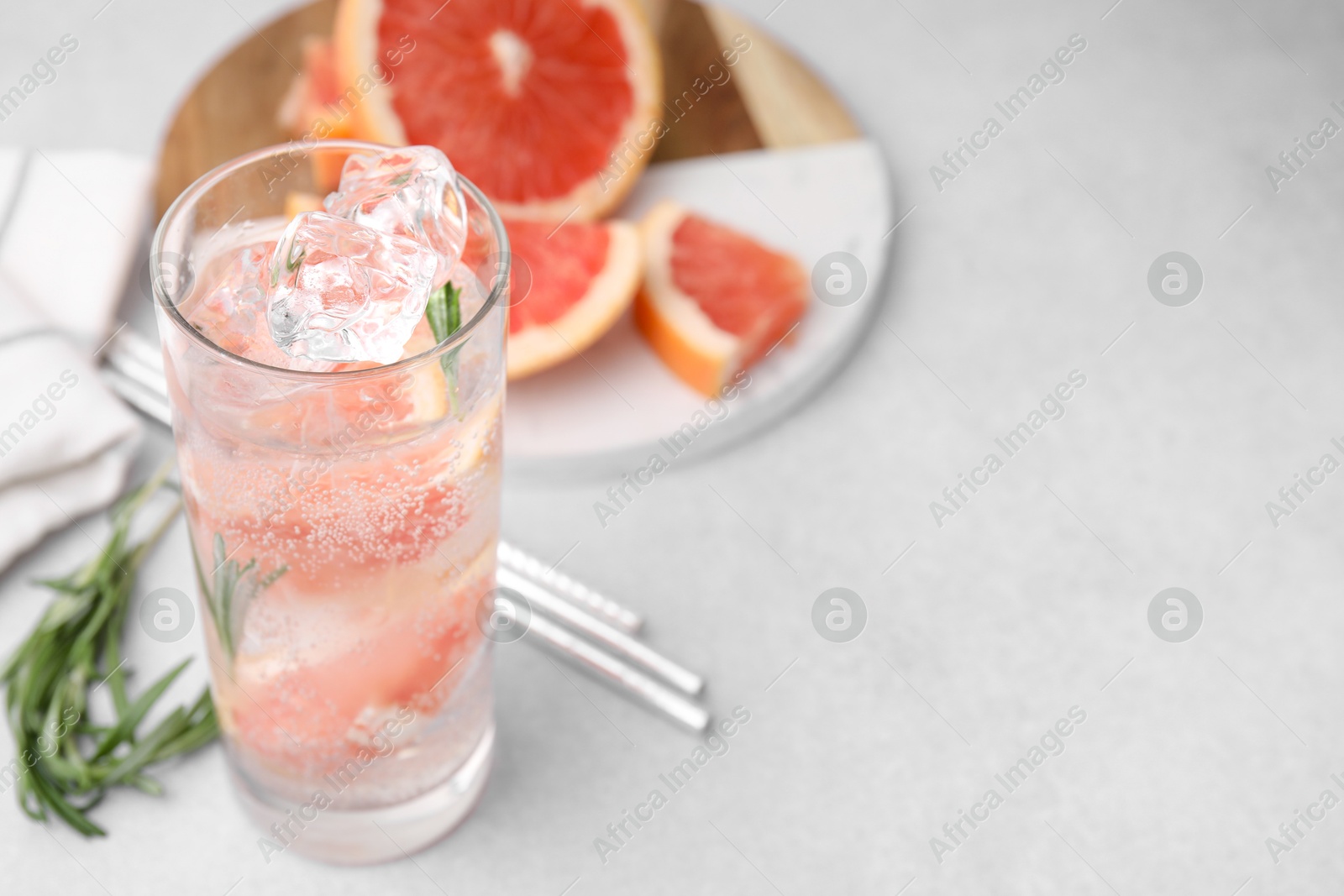 Photo of Refreshing water with grapefruit and rosemary in glass on light table, closeup. Space for text