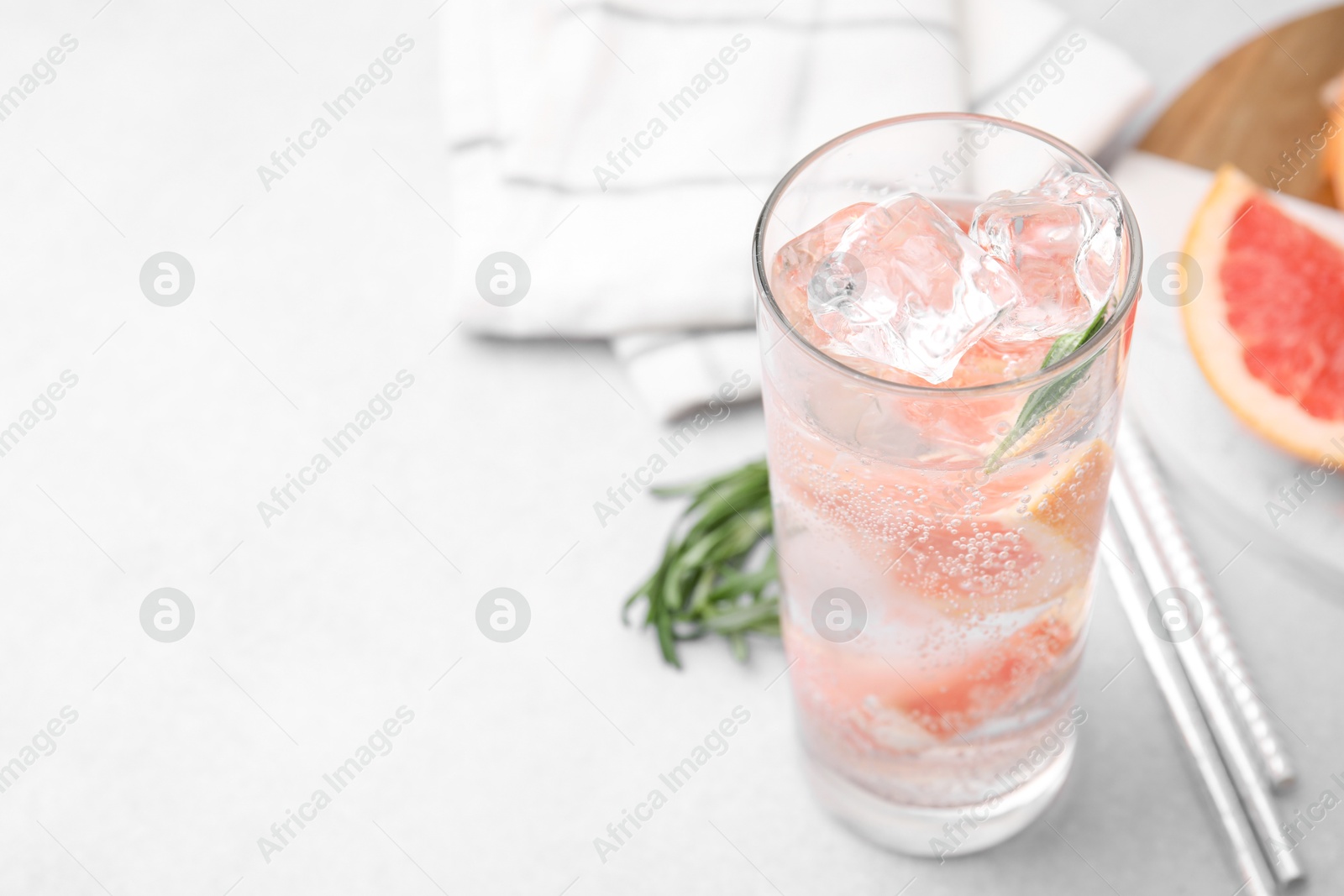 Photo of Refreshing water with grapefruit and rosemary in glass on light table, closeup. Space for text