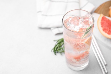 Photo of Refreshing water with grapefruit and rosemary in glass on light table, closeup. Space for text