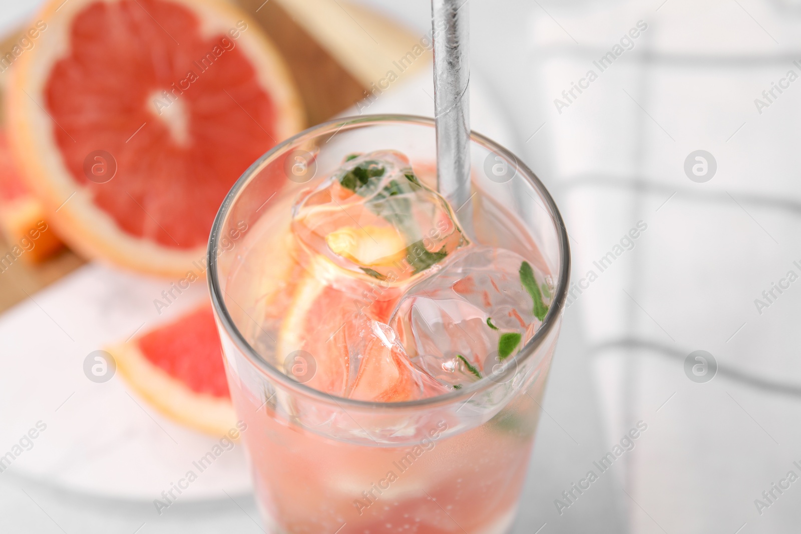 Photo of Refreshing water with grapefruit and rosemary in glass on light table, closeup