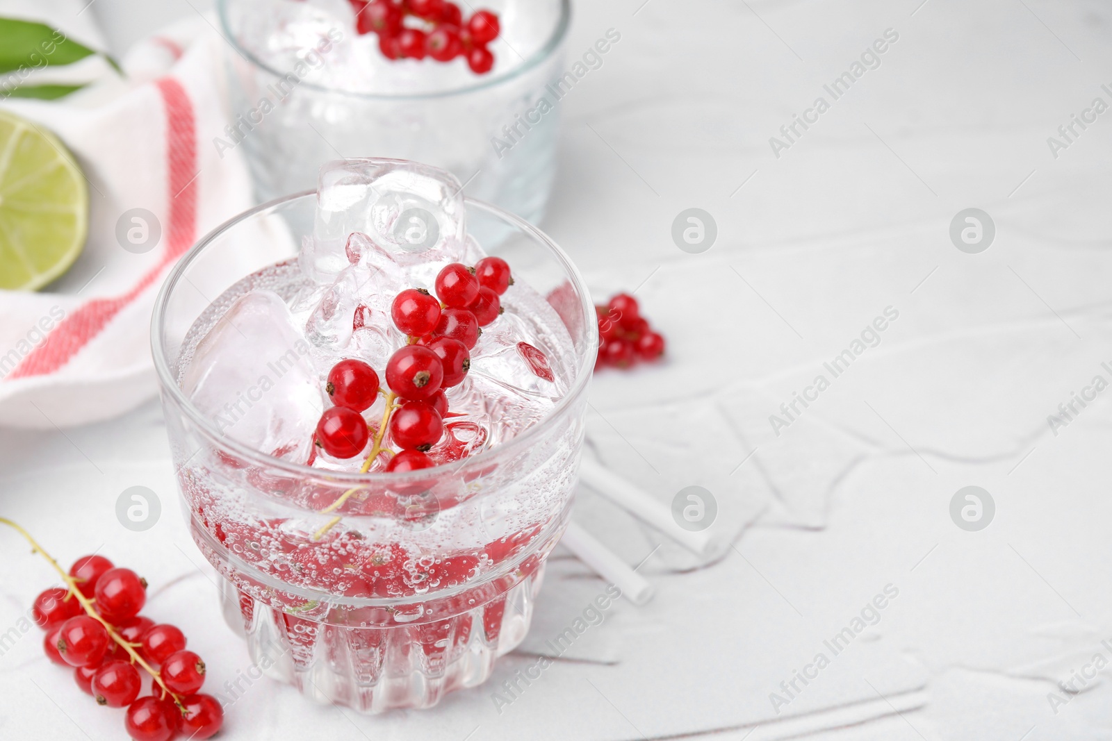 Photo of Refreshing water with red currants in glass on light table, closeup. Space for text