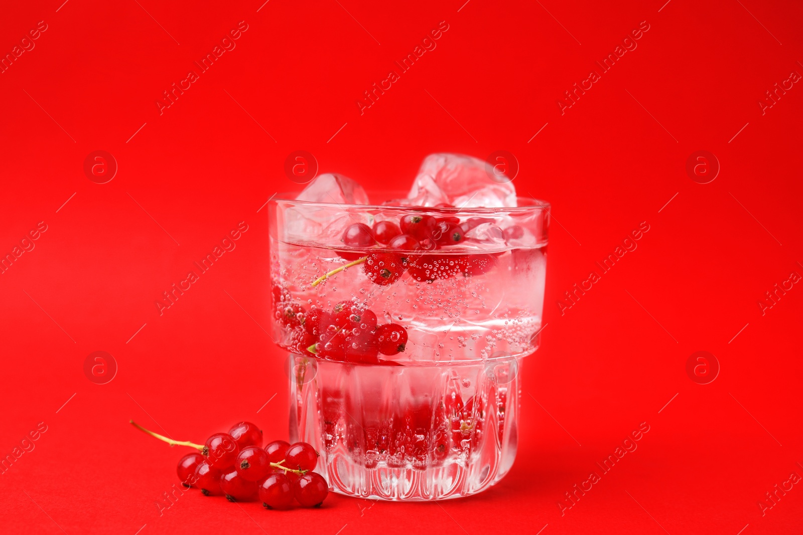 Photo of Refreshing water with red currants and mint in glass on red background