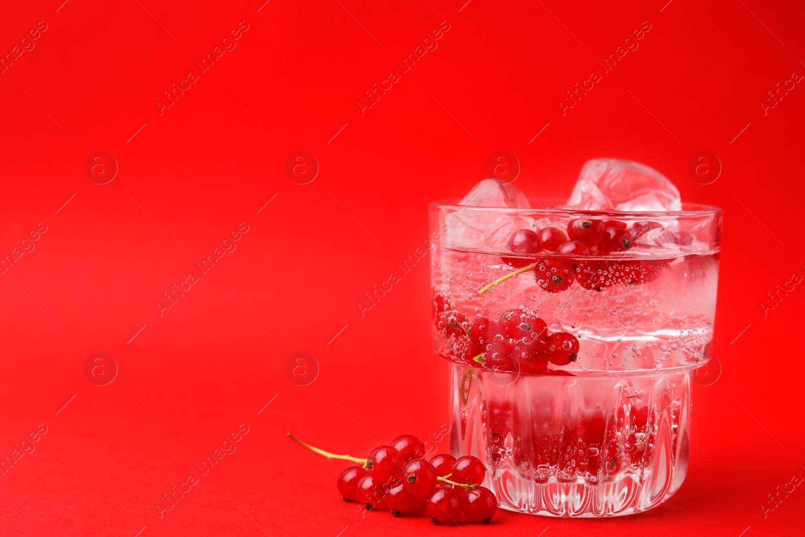 Photo of Refreshing water with red currants and mint in glass on red background, space for text