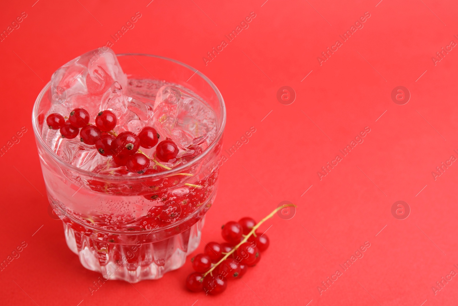 Photo of Refreshing water with red currants and mint in glass on red background, closeup. Space for text