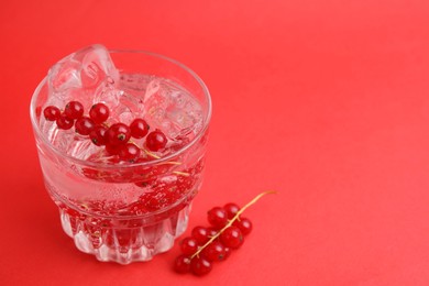 Photo of Refreshing water with red currants and mint in glass on red background, closeup. Space for text