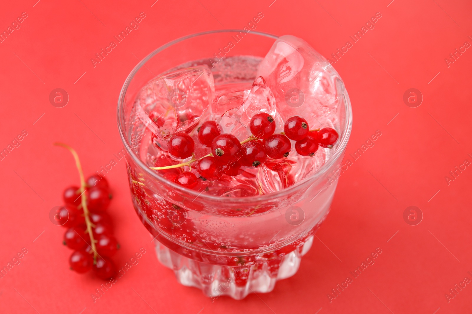 Photo of Refreshing water with red currants and mint in glass on red background, closeup