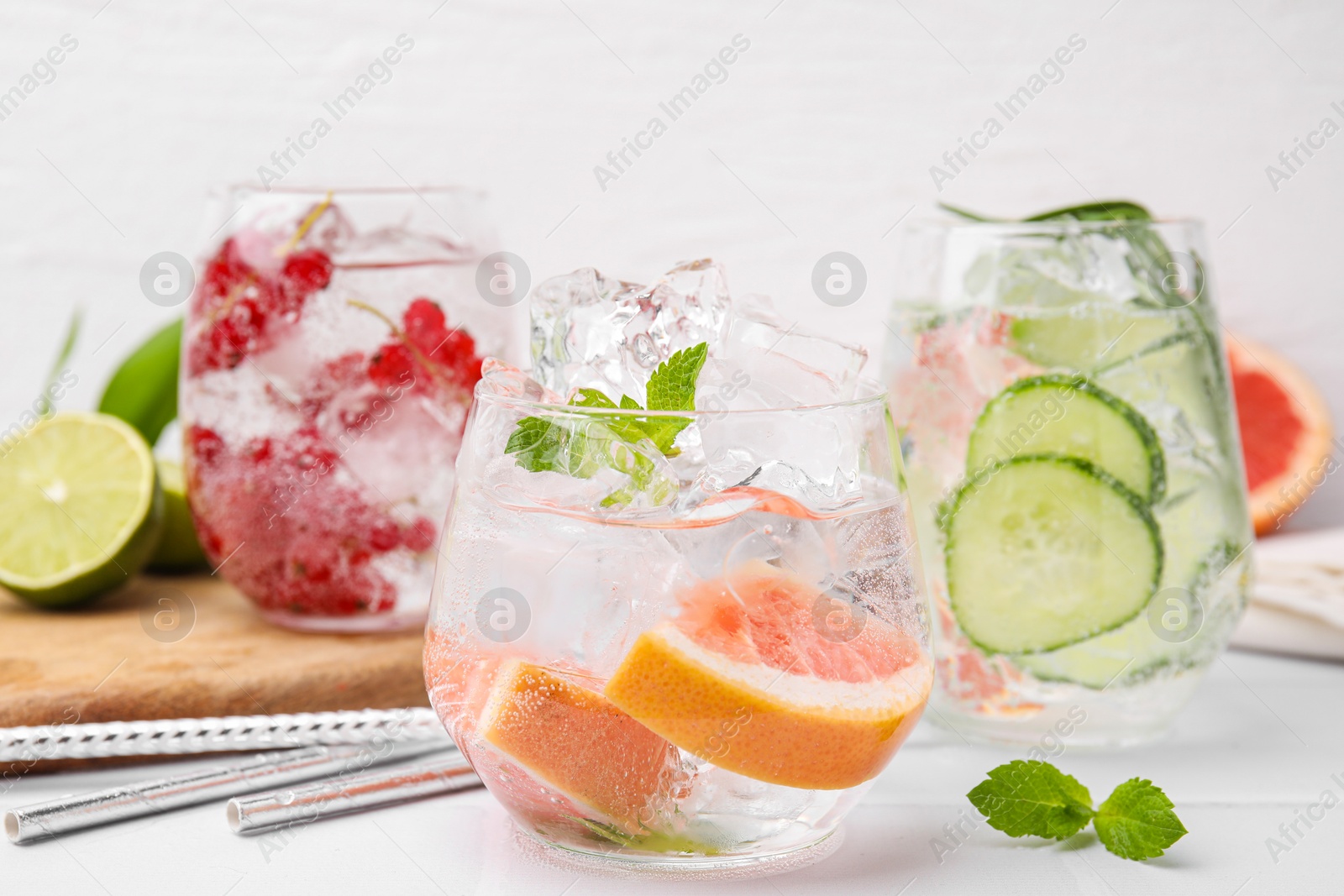 Photo of Different refreshing drinks in glasses on white tiled table, closeup