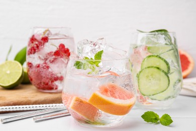 Photo of Different refreshing drinks in glasses on white tiled table, closeup