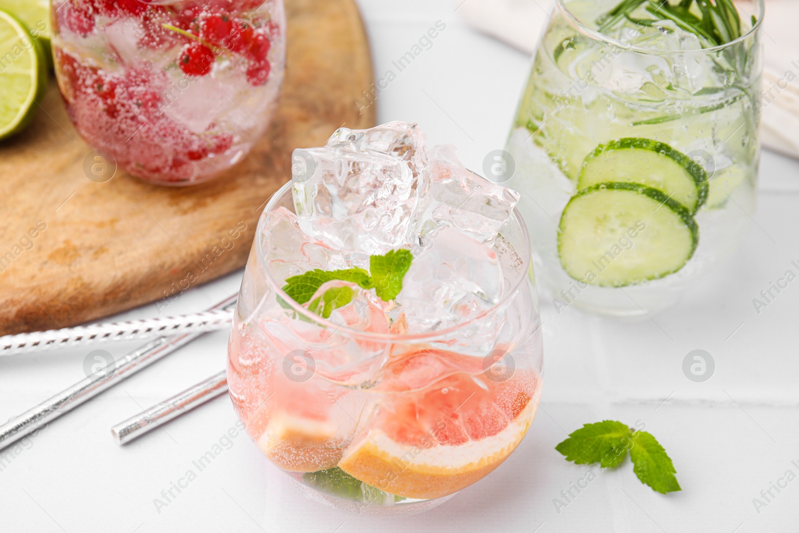 Photo of Different refreshing drinks in glasses on white tiled table, closeup