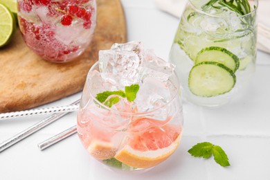 Photo of Different refreshing drinks in glasses on white tiled table, closeup