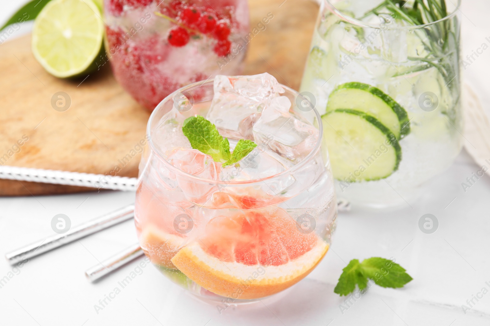 Photo of Different refreshing drinks in glasses on white tiled table, closeup