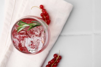 Photo of Refreshing water with red currants and rosemary in glass on white tiled table, top view. Space for text