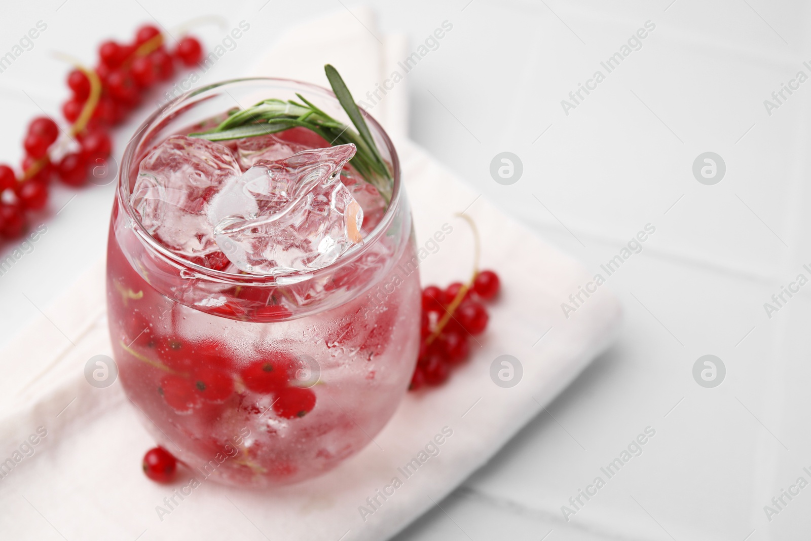 Photo of Refreshing water with red currants and rosemary in glass on white tiled table, closeup. Space for text