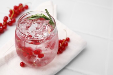 Photo of Refreshing water with red currants and rosemary in glass on white tiled table, closeup. Space for text