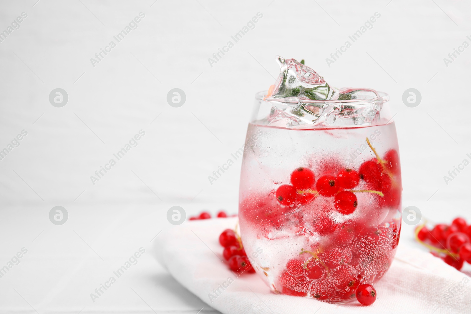 Photo of Refreshing water with red currants in glass on white table, space for text