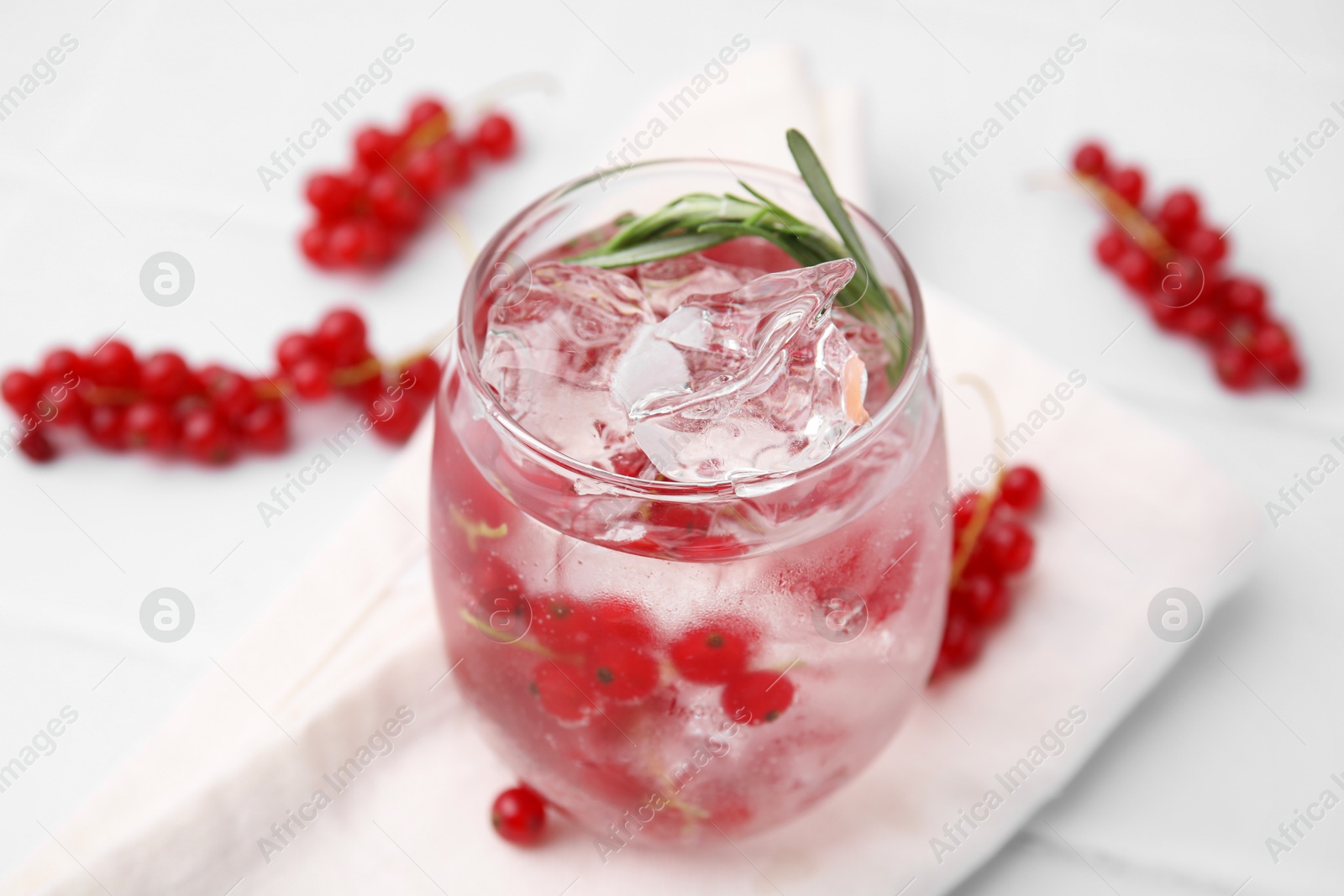 Photo of Refreshing water with red currants and rosemary in glass on white tiled table, closeup