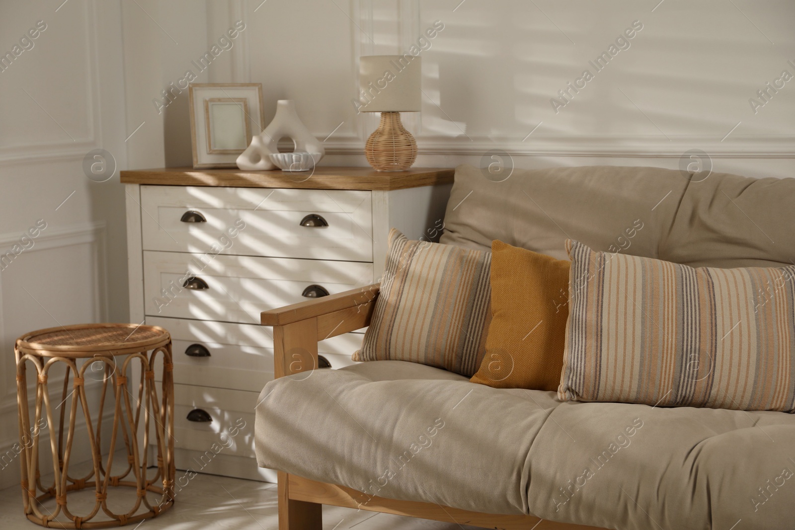 Photo of Sofa with soft pillows, chest of drawers, different decorative elements and side table indoors