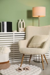 Beige armchair with soft pillow, slippers and different decorative elements indoors