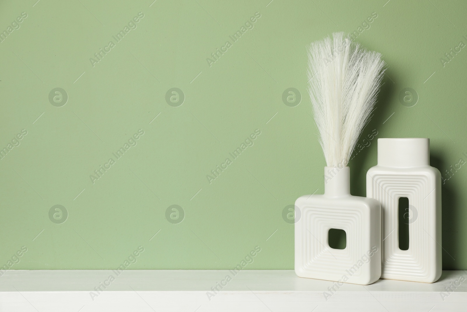 Photo of Beautiful decorative plants and vases on white shelf near green wall indoors, space for text