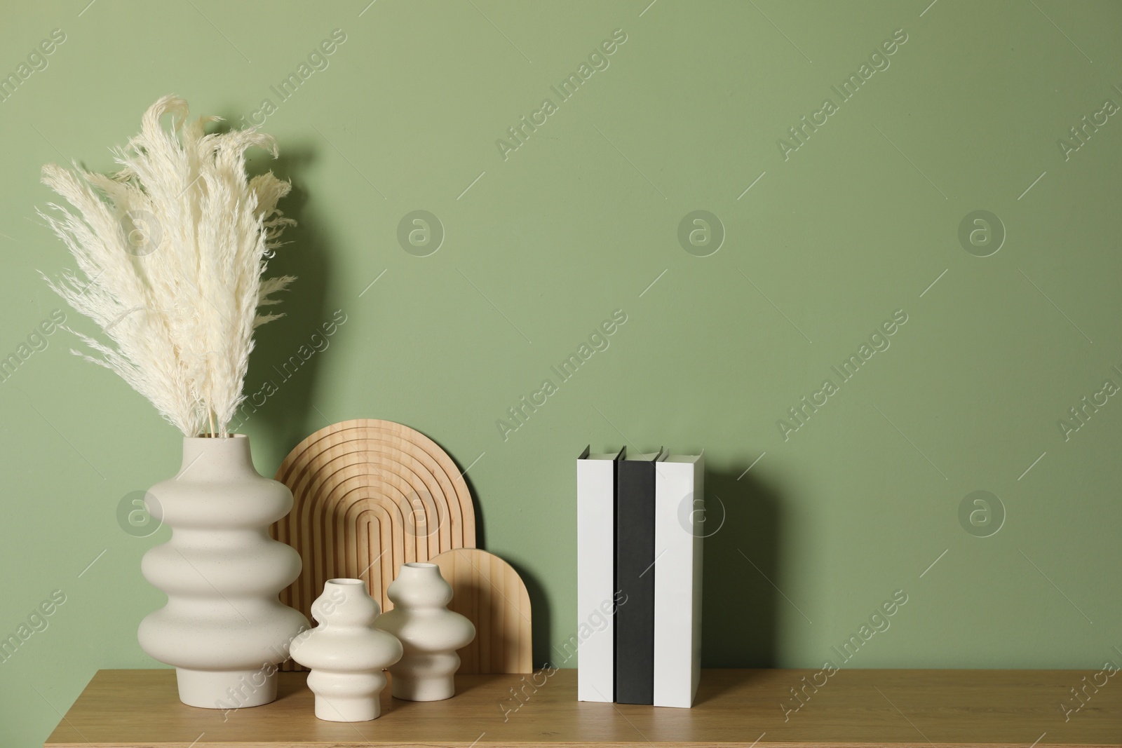 Photo of Beautiful decorative plants, vases, wooden boards and hardcover books with different cities names on table near green wall indoors, space for text