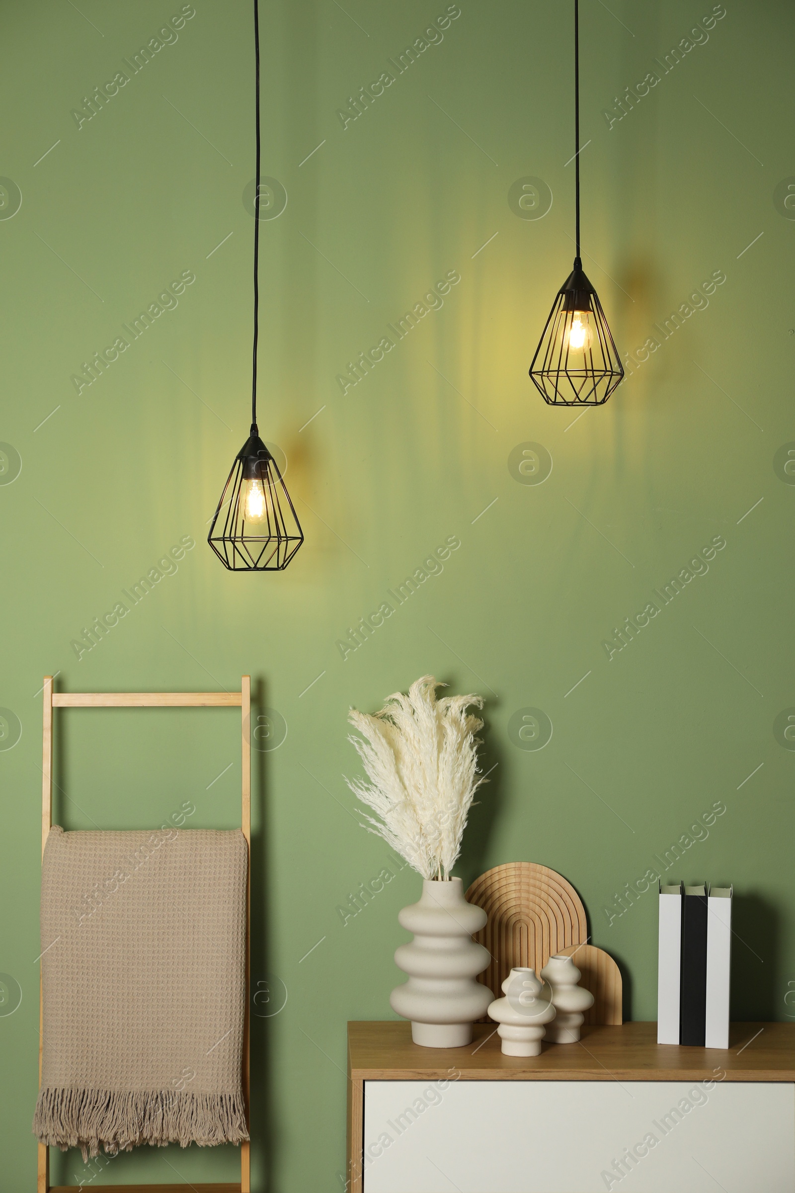 Photo of Different decorative elements on chest of drawers and blanket near green wall indoors