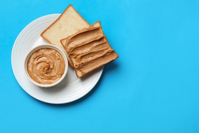 Photo of Delicious sandwich with peanut butter and tasty paste in bowl on light blue table, top view. Space for text