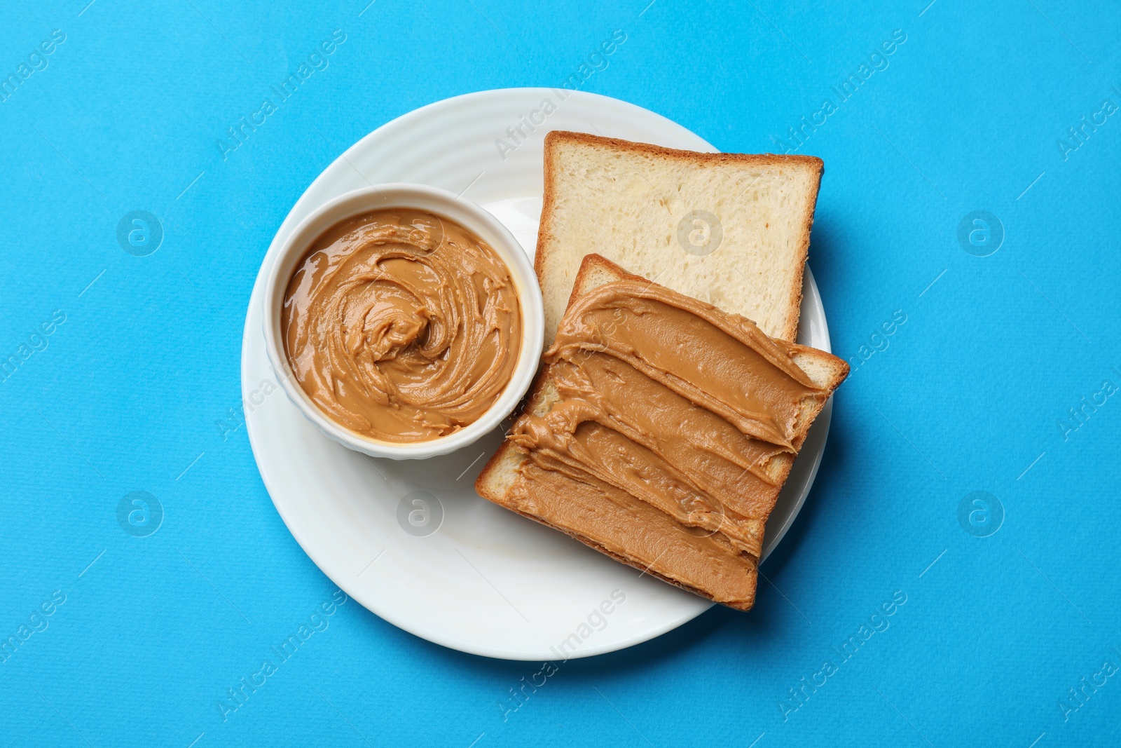 Photo of Delicious sandwich with peanut butter and tasty paste in bowl on light blue table, top view