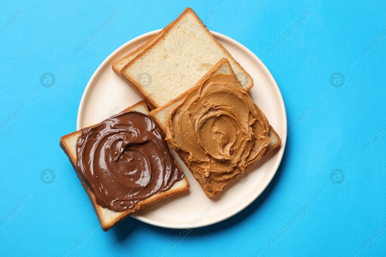 Photo of Delicious sandwiches with peanut butter and chocolate paste on light blue table, top view