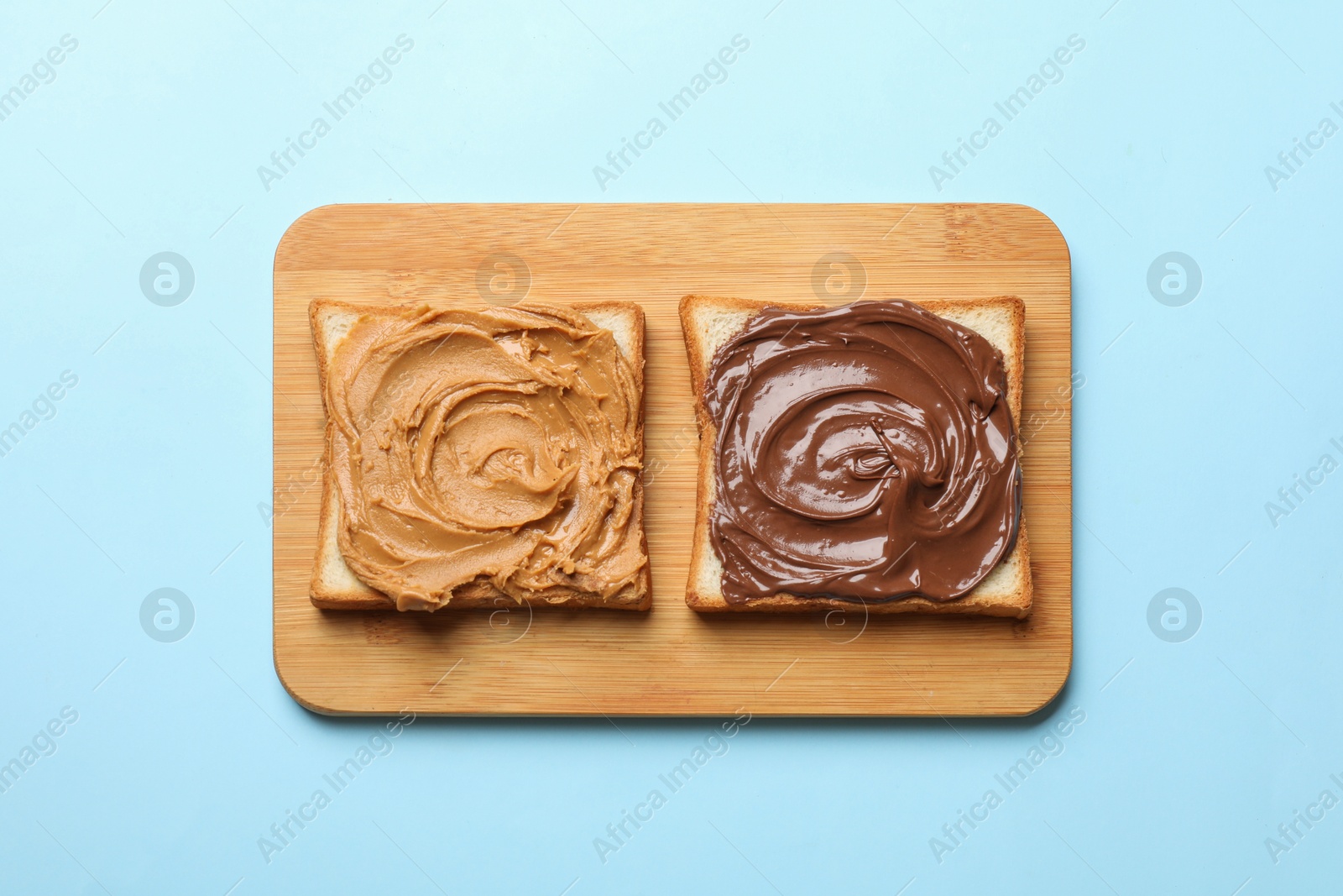 Photo of Delicious sandwiches with peanut butter and chocolate paste on light blue table, top view